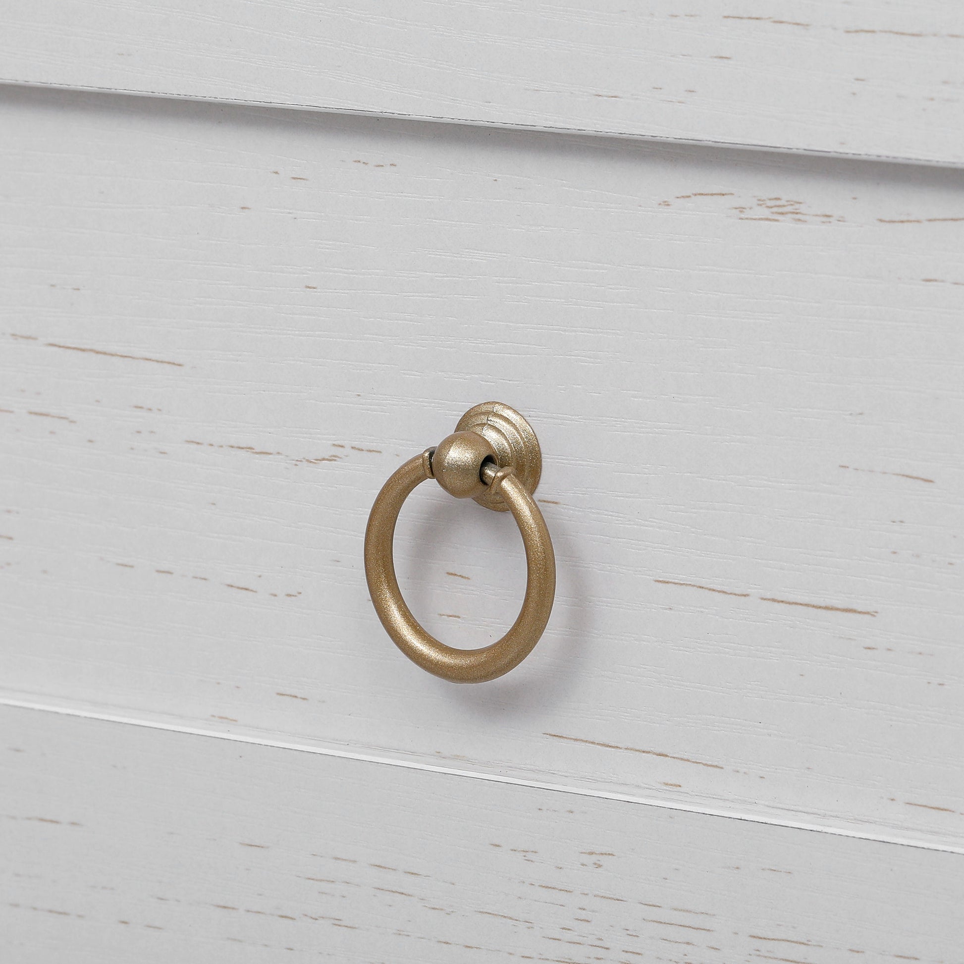 Close-up detail of the gold ring drawer handle on the white Artisan farmhouse pantry cabinet with distressed wood grain finish