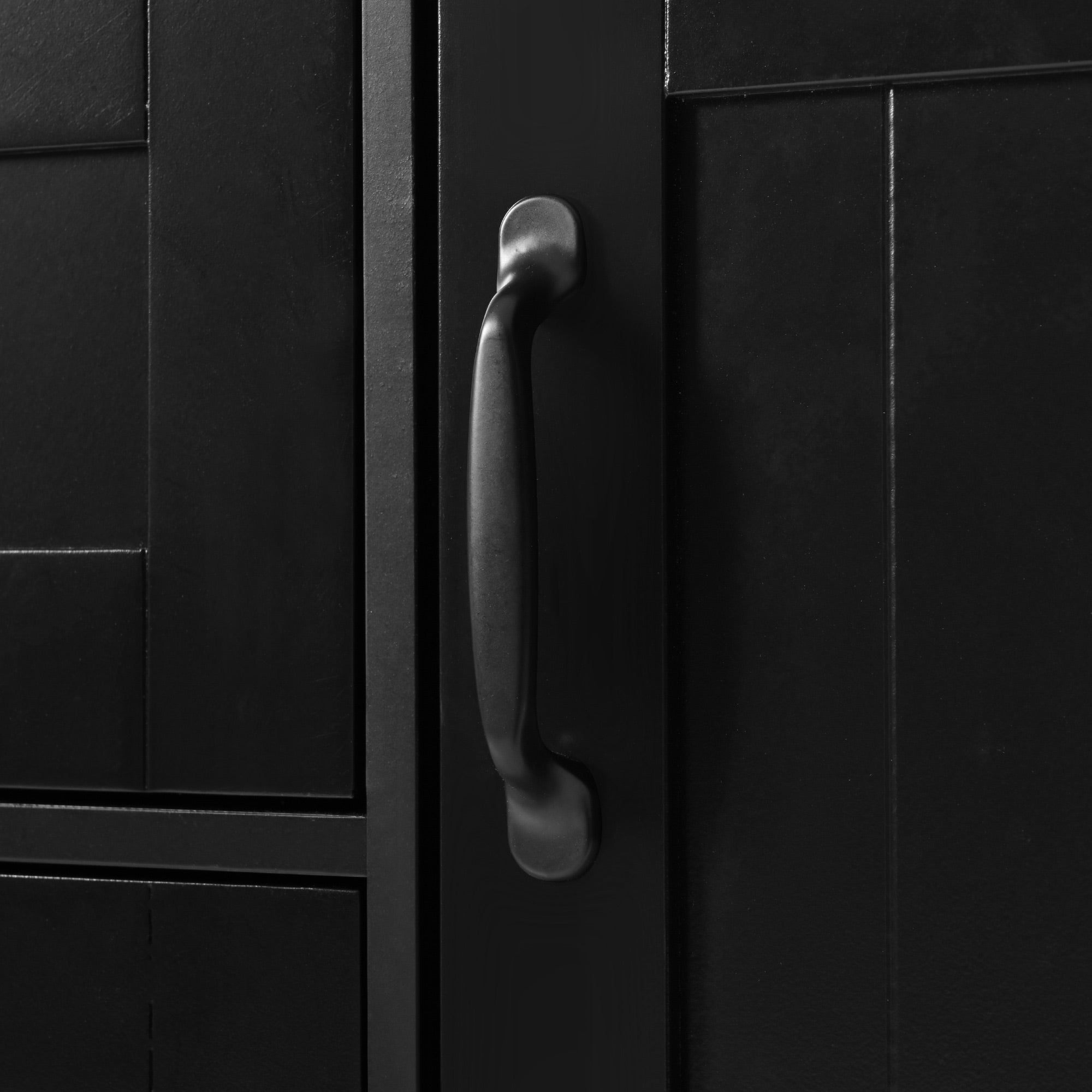 Close-up detail of the BRYNNA black kitchen island featuring matte black metal cabinet handles and farmhouse-style paneled door design