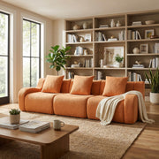 Chico orange 3-seater sofa in cozy living room with wood shelves and neutral decor