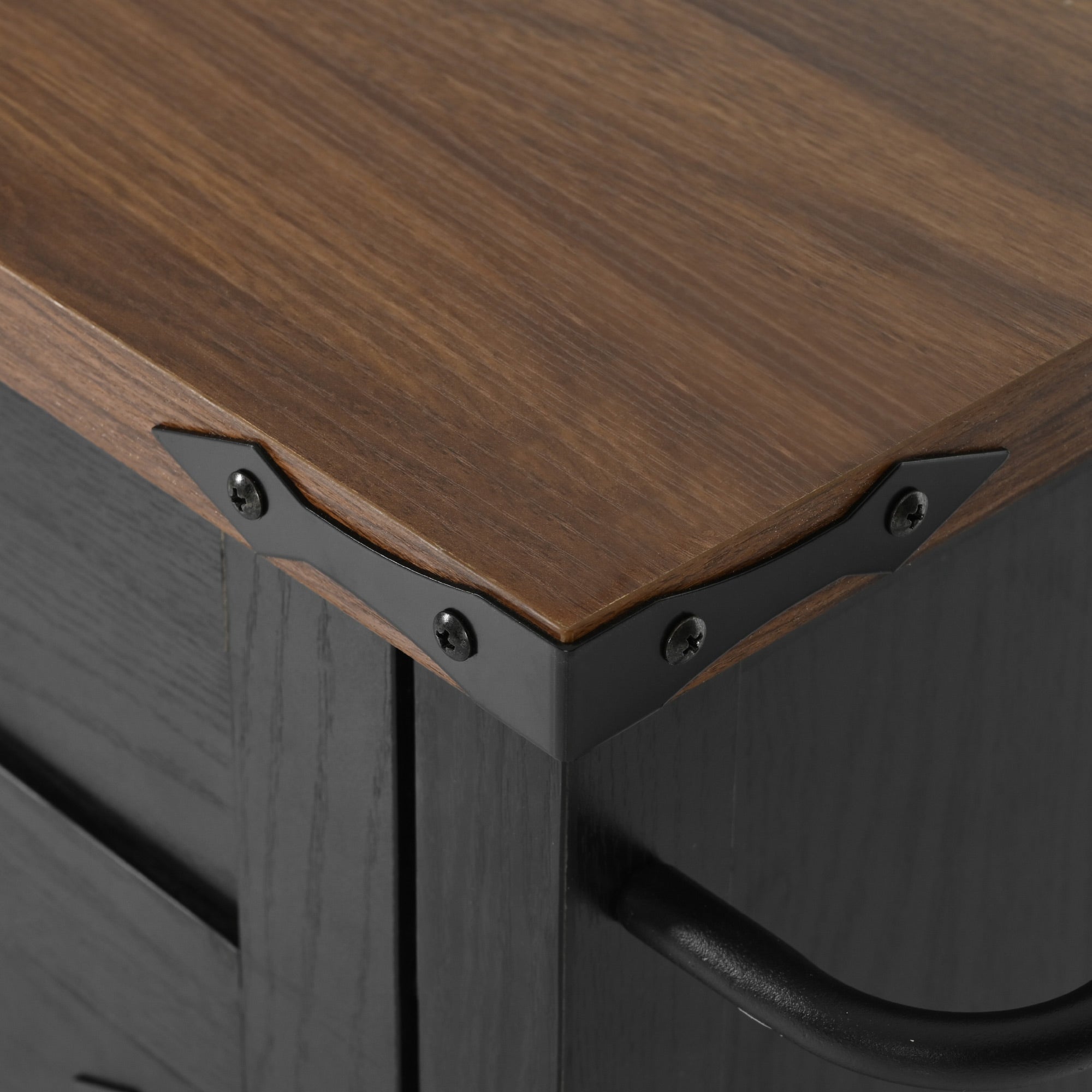 Close-up detail of rustic wood grain countertop corner and black metal trim on black Dijon farmhouse rolling kitchen island isolated on white background