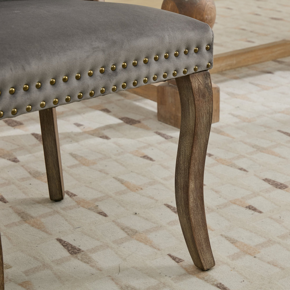 Elbe gray dining chair showing curved solid wood leg and antique brass nailhead trim detail