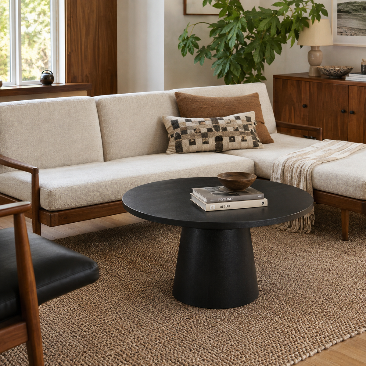 Genoa black pedestal coffee table beside a cream sofa in a warm living room setting