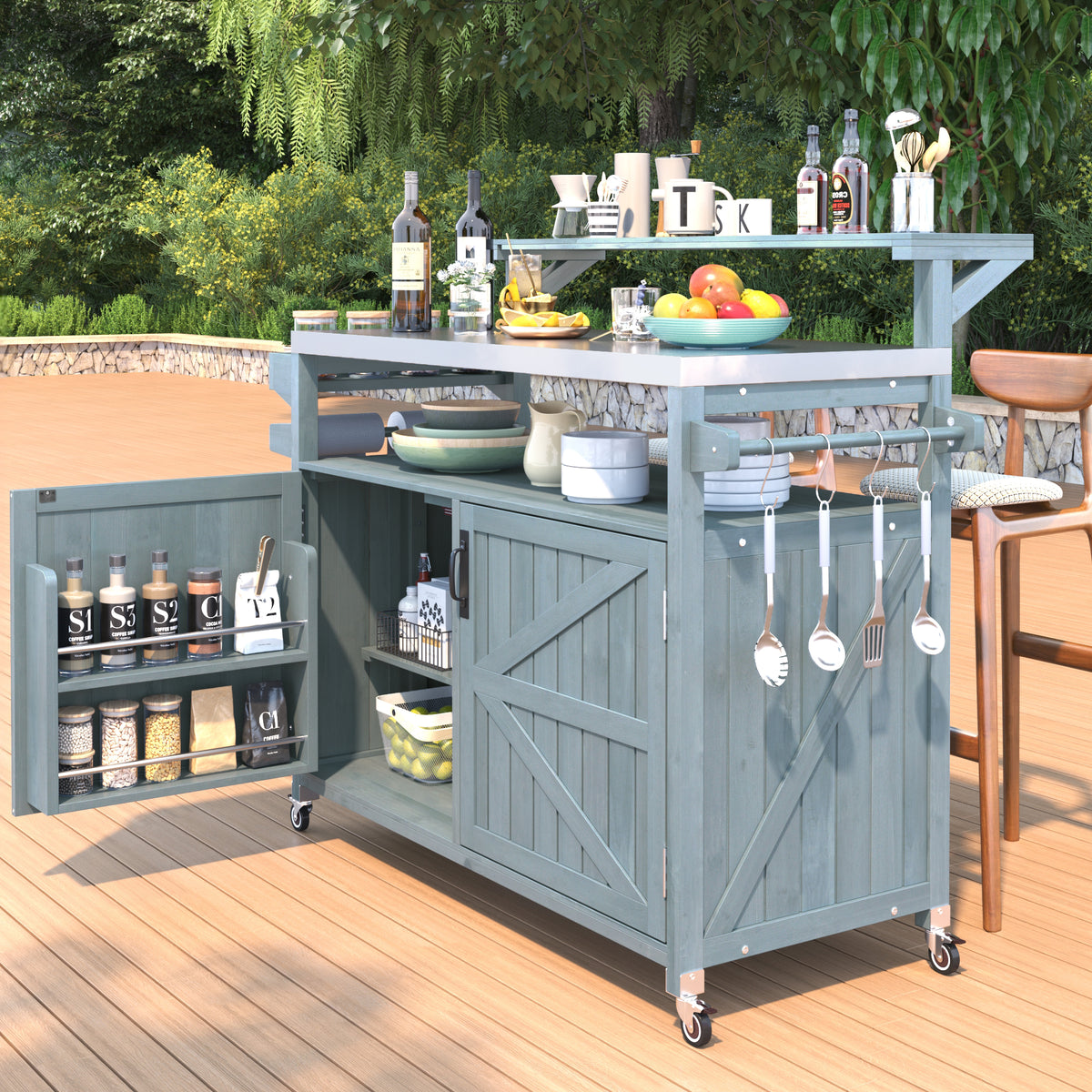 Gray blue Limoges rolling outdoor kitchen island with stainless steel countertop open cabinet storage spice rack utensil hooks and caster wheels styled on an outdoor patio deck