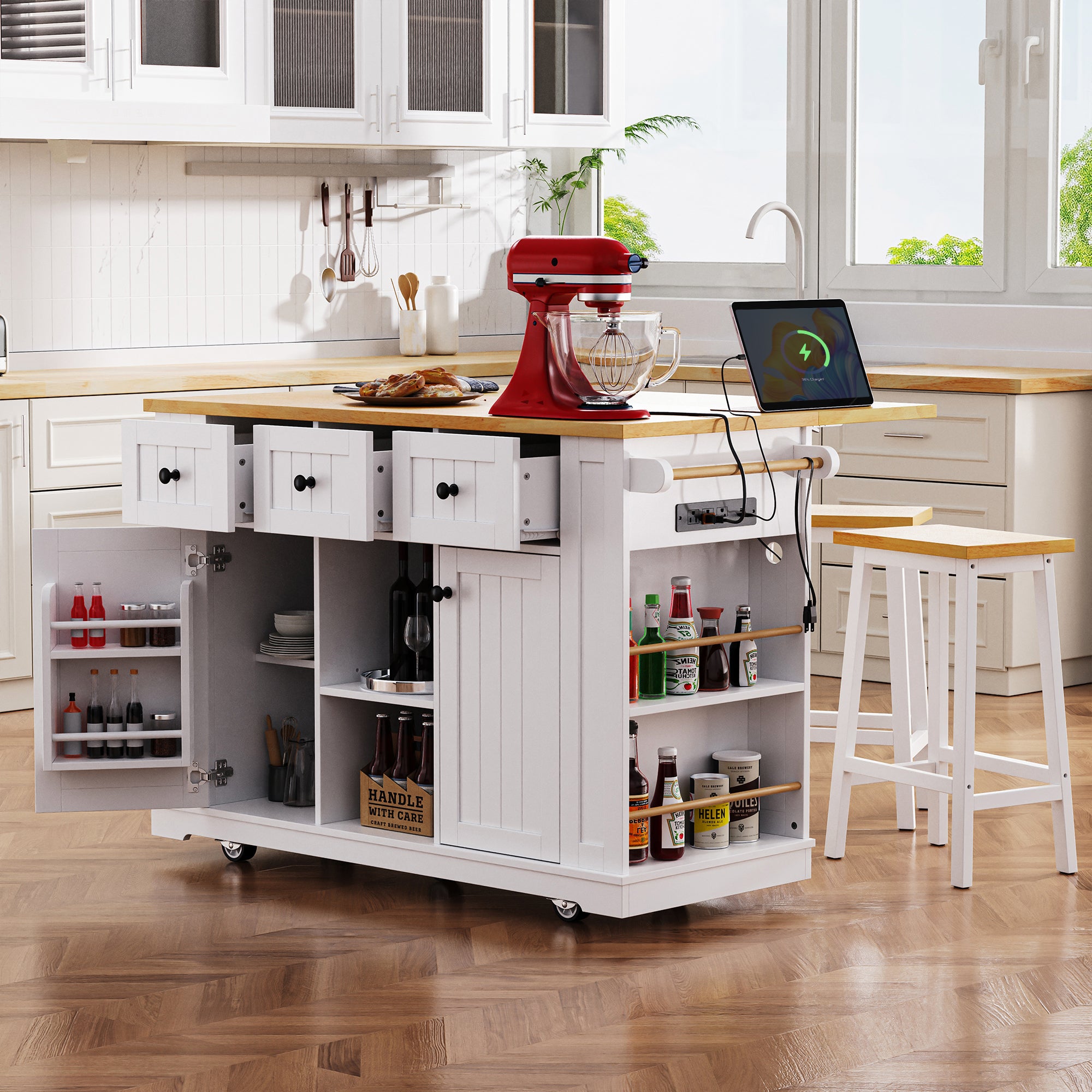 Maui white rolling kitchen island with expandable drop leaf countertop open side shelves power outlet drawers cabinet storage and matching stools in modern kitchen scene