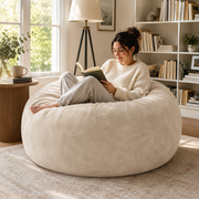 Pebble beige bean bag chair showing a woman reading in a bright living room beside a large window