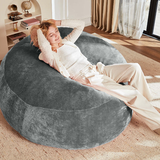 Pebble dark grey bean bag chair showing a woman reclining in a warm neutral living room