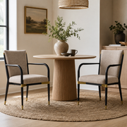 Trasimeno black upholstered dining armchairs with brass-tone accents around a round wood dining table
