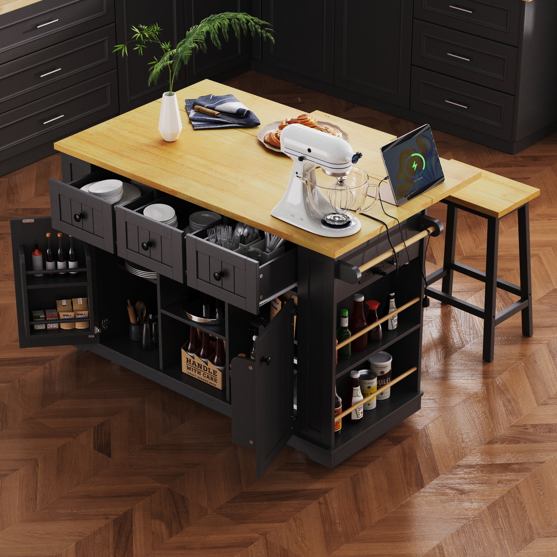 Top angle view of Maui black rolling kitchen island with open drawers cabinet storage side spice racks built in power outlet and extended drop leaf countertop in kitchen setting